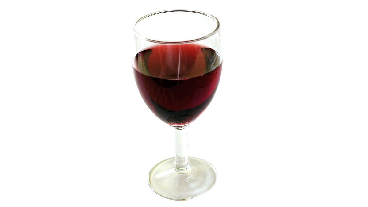 A stemmed glass of deep red wine standing against a plain white background, showing the colour fading toward the rim.
