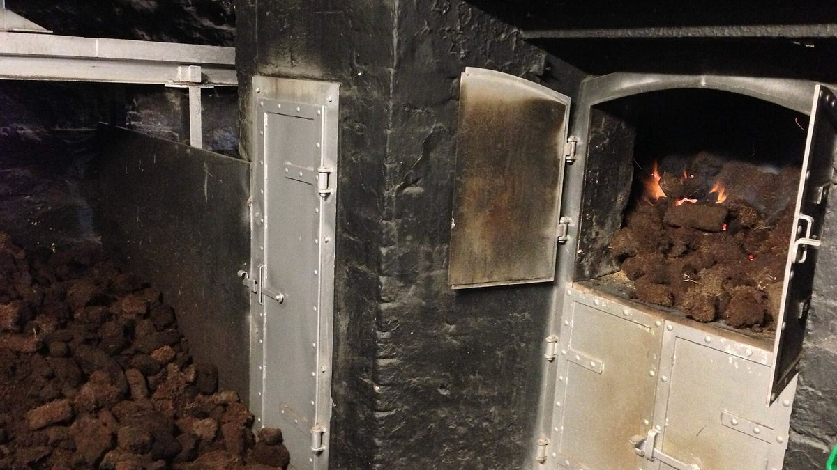 Blocks of peat burning in an open kiln furnace, with more peat stacked beside it.