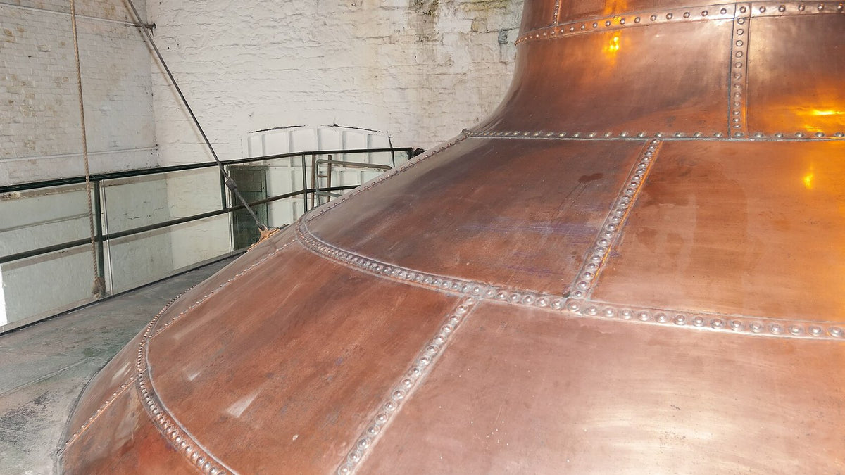 The riveted copper base of a giant pot still inside an old Irish distillery.