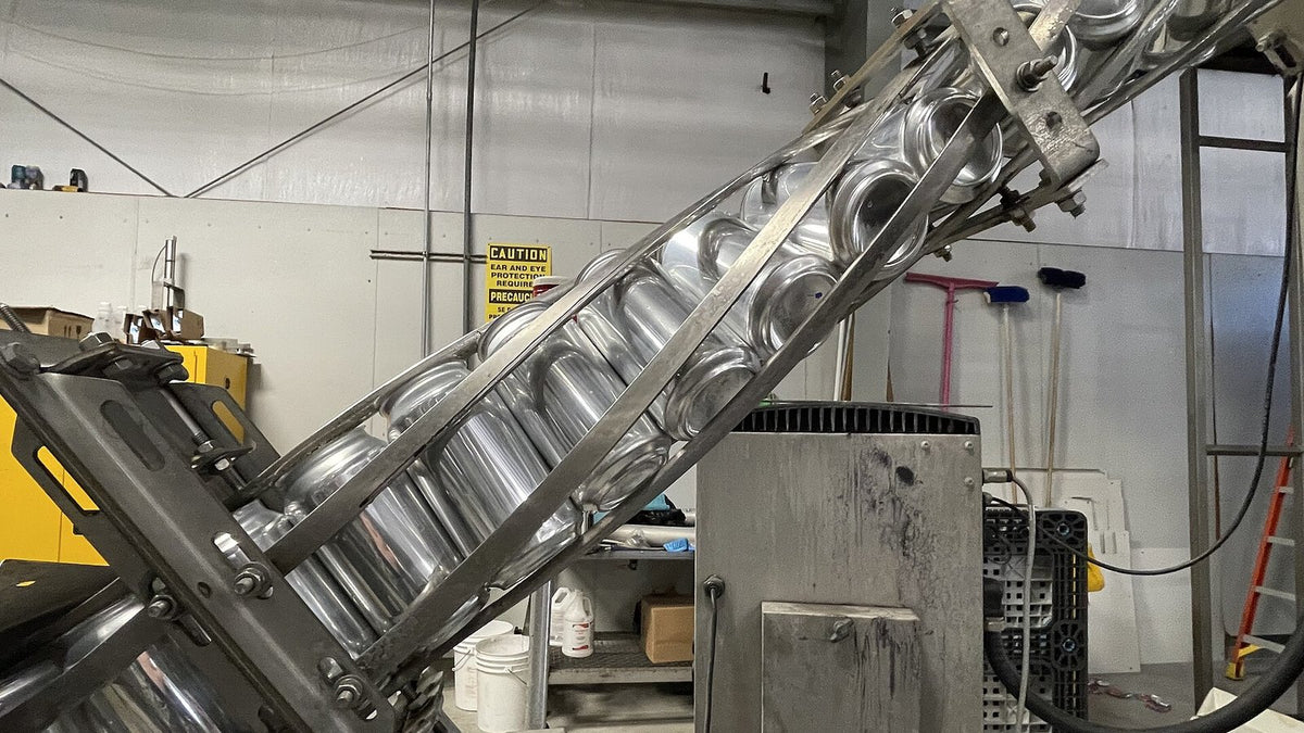 Empty unprinted aluminium cans riding an inclined conveyor into a canning line.