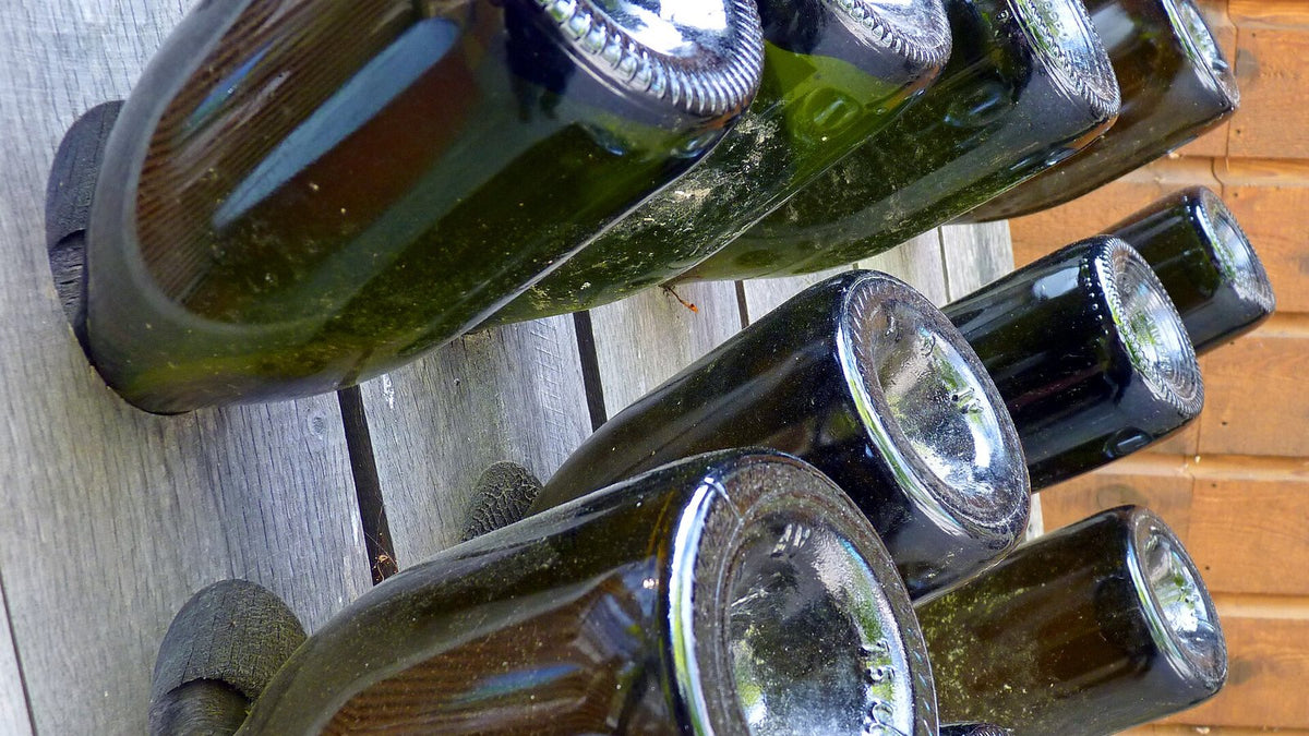 Necks of sparkling-wine bottles angled downward in the holes of a wooden riddling rack.
