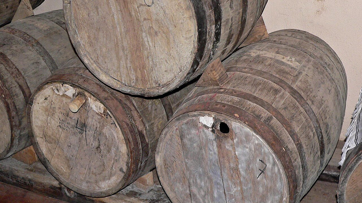 Weathered oak barrels stacked on their sides in a tequila hacienda aging room.