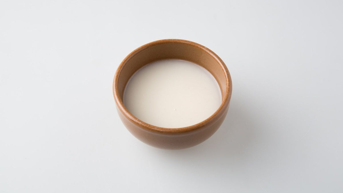 A brown ceramic bowl of milky white makgeolli on a plain white surface.