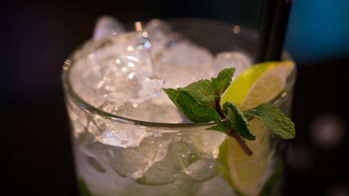 Close-up of an alcohol-free drink over crushed ice, garnished with a sprig of mint and a lime wedge, against a dark bar.