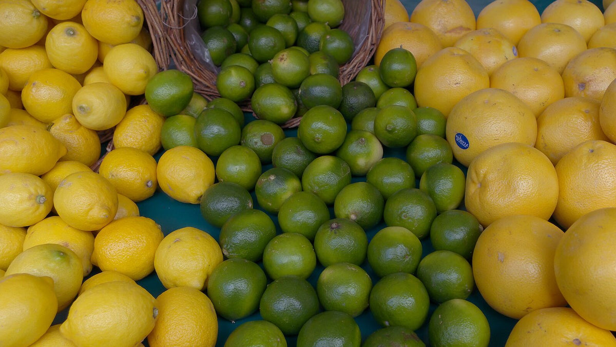 A market display of lemons, limes and pomelos with a woven basket of limes tipped over.