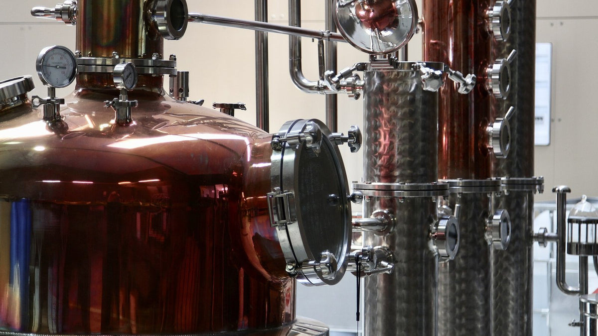 A copper pot still with a porthole joined to stainless-steel distillation columns with sight glasses.