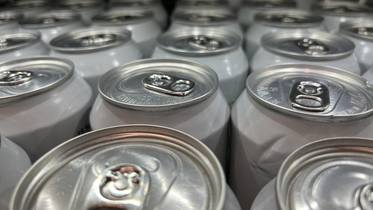 Close-up of the tops of rows of plain white aluminium drink cans with ring-pull tabs.
