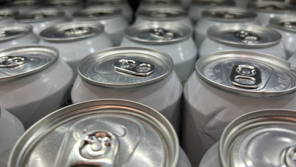 Close-up of the tops of rows of plain white aluminium drink cans with ring-pull tabs.