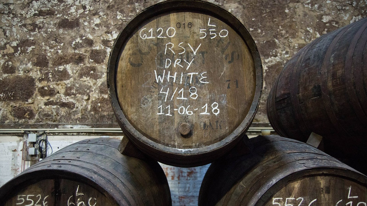 Old port casks with chalked lot numbers and dates stacked against a stone wall.