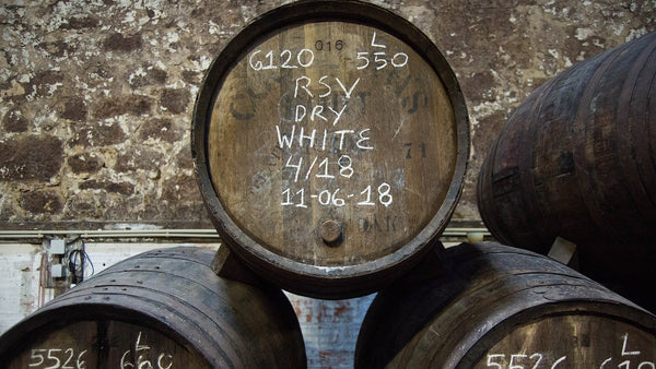 Old port casks with chalked lot numbers and dates stacked against a stone wall.