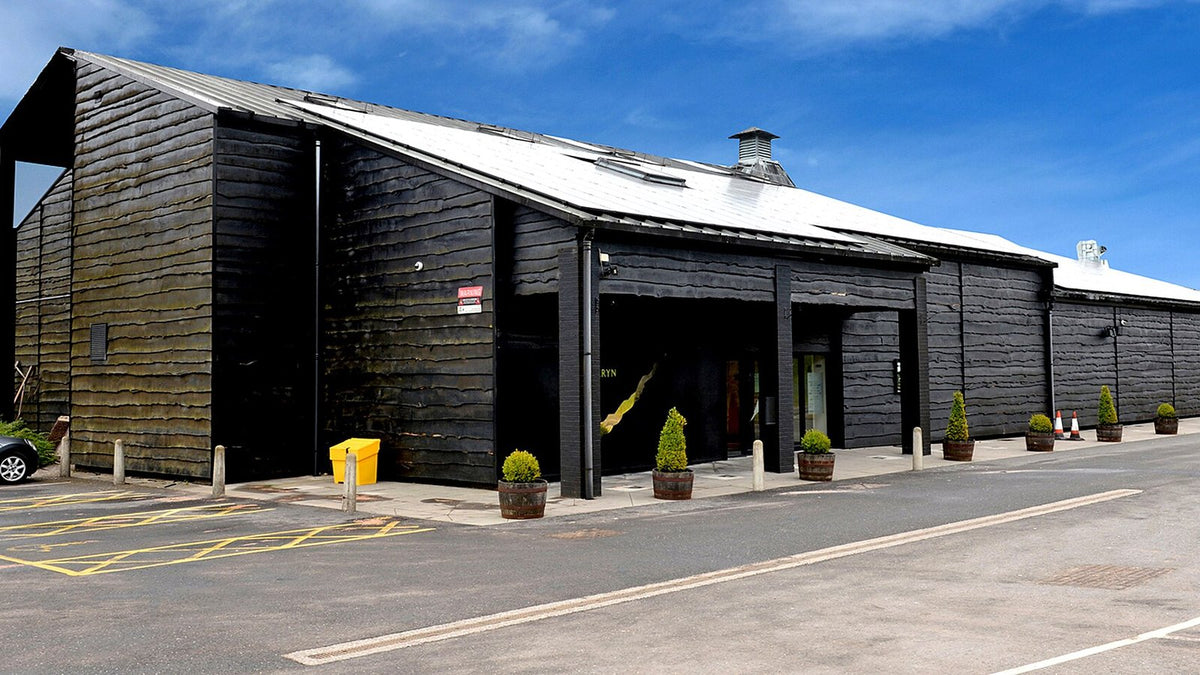 A black timber-clad distillery building under a blue sky in South Wales.