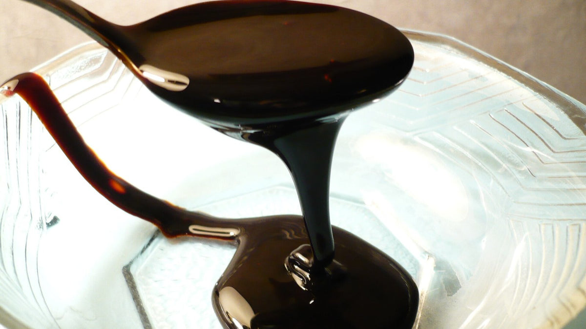 Thick blackstrap molasses pouring from a spoon into a glass dish.