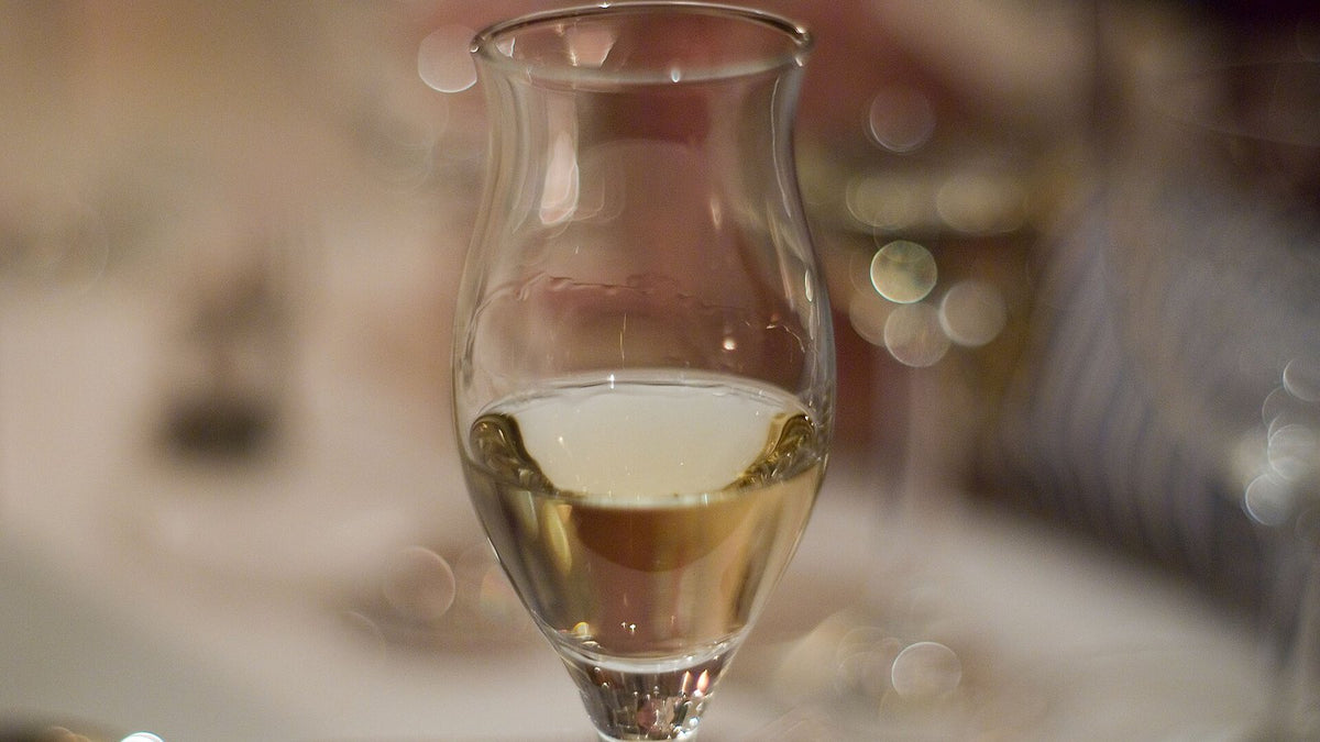 A stemmed tulip glass of nearly clear spirit on a softly blurred table.