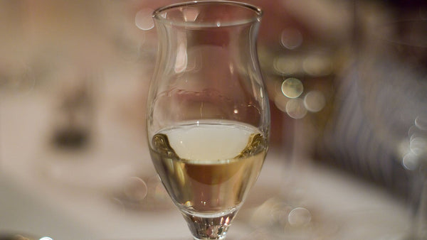A stemmed tulip glass of nearly clear spirit on a softly blurred table.