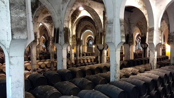 Rows of dark oak casks stacked under whitewashed arches in a large Jerez bodega.