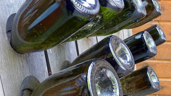 Necks of sparkling-wine bottles angled downward in the holes of a wooden riddling rack.