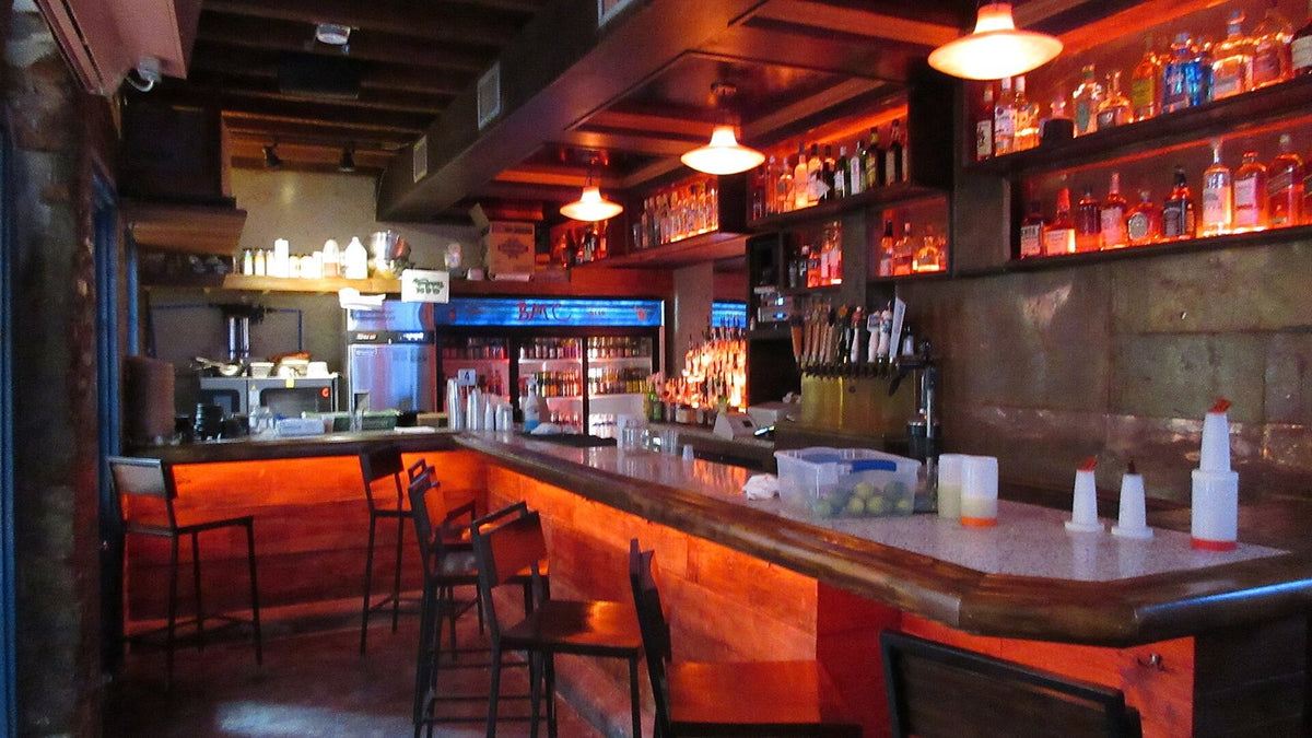 An empty bar with red under-lit counter, stools and backlit shelves of bottles too distant to read.