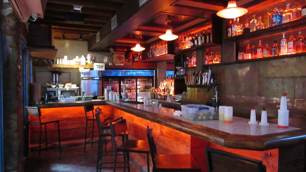 An empty bar with red under-lit counter, stools and backlit shelves of bottles too distant to read.
