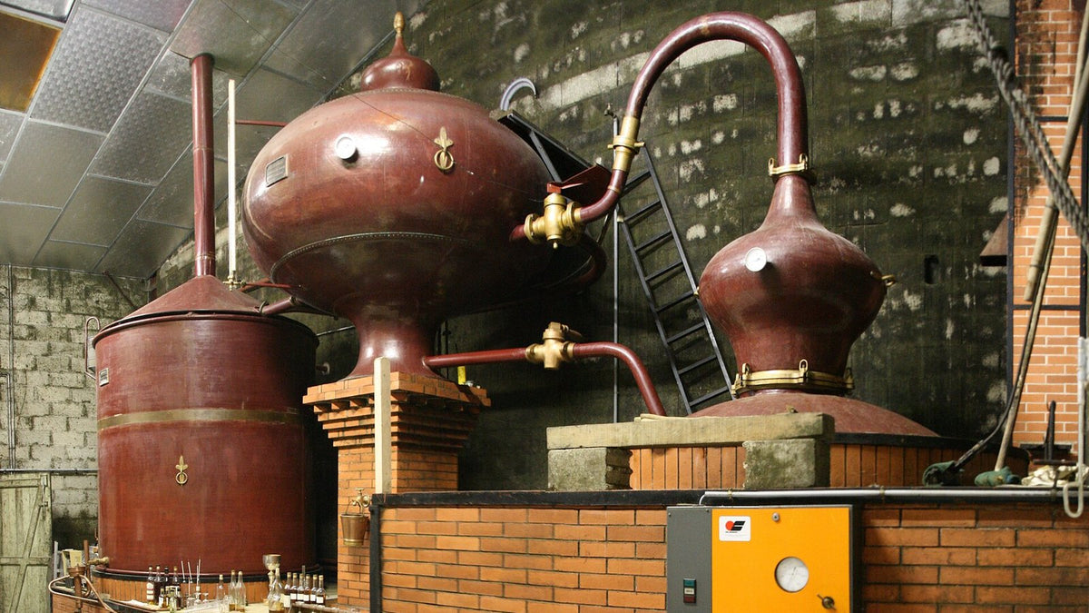 A Charentais copper pot still with its onion-shaped wine preheater, set in a brick furnace inside a distillery.