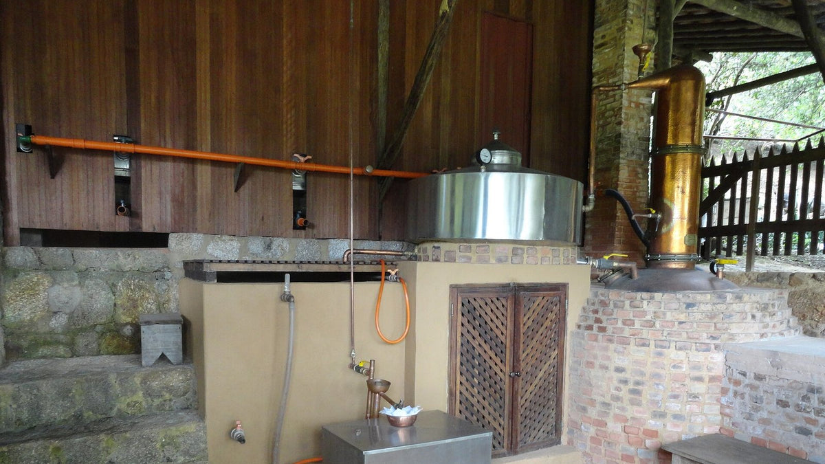 Small cachaça distillery in Paraty, Brazil, with a copper alembic column beside a stainless pot and brick furnace.