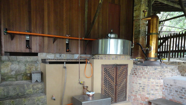 Small cachaça distillery in Paraty, Brazil, with a copper alembic column beside a stainless pot and brick furnace.