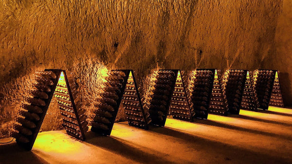 Wooden riddling racks of sparkling-wine bottles lit amber inside a carved chalk cellar in Reims.