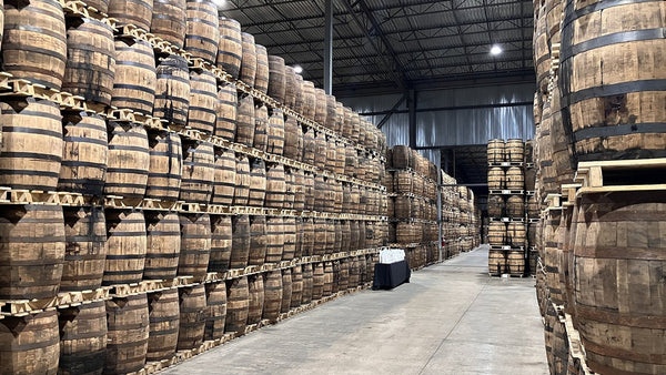 Tall stacks of palletised whisky barrels lining an aisle in an Ontario maturation warehouse.