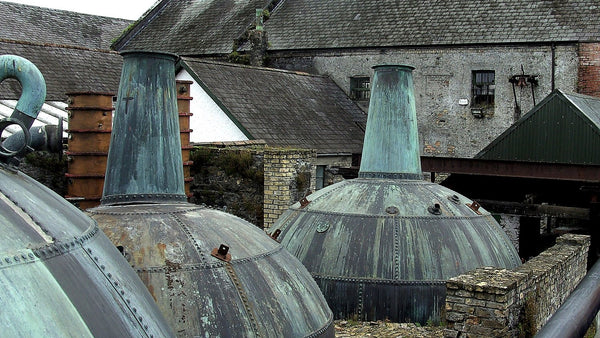 Weathered green-patina copper pot stills in the yard of an old Irish distillery.