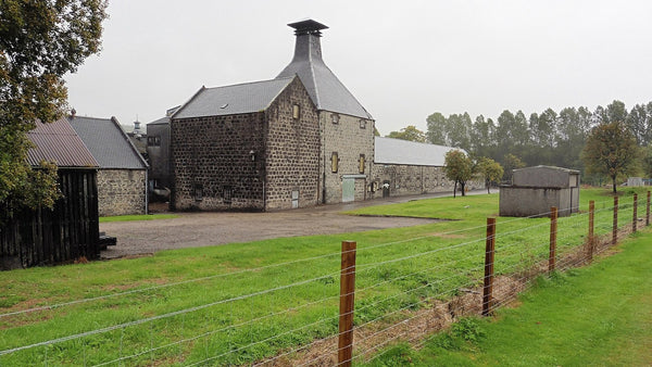 A stone malt kiln with a pagoda-style vent beside green fields at a Speyside distillery.
