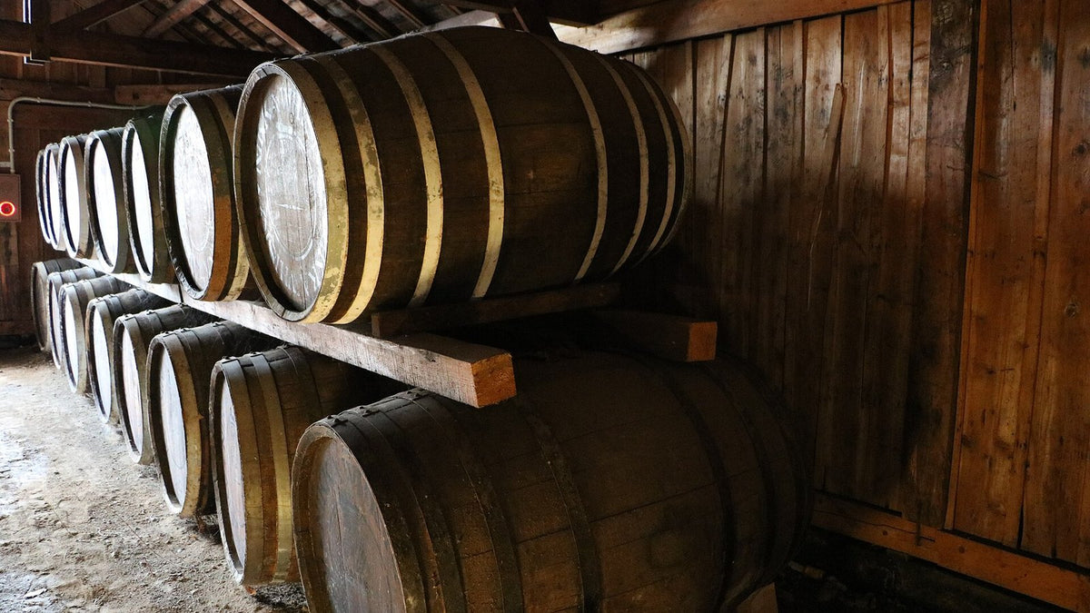 Oak whisky casks resting on wooden racks in a dim timber-walled warehouse.