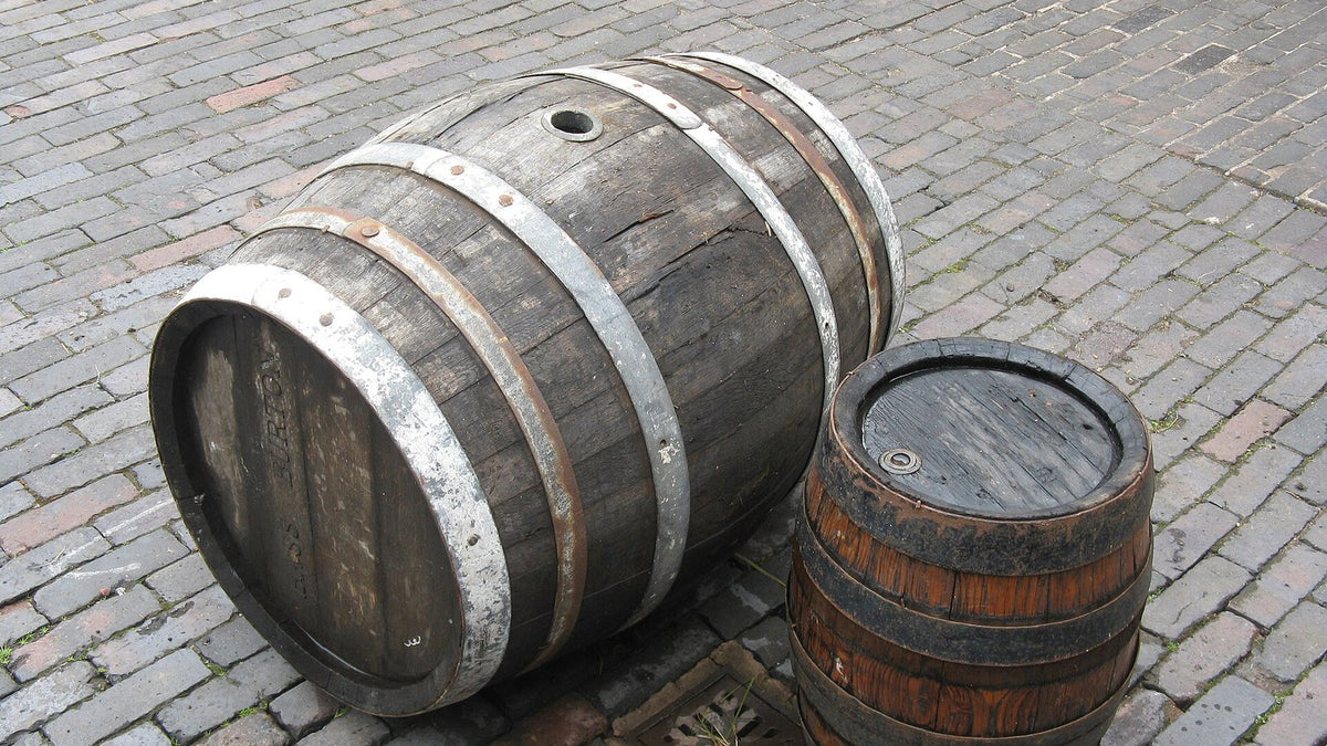 A single weathered oak cask lying on cobblestones next to a small keg.