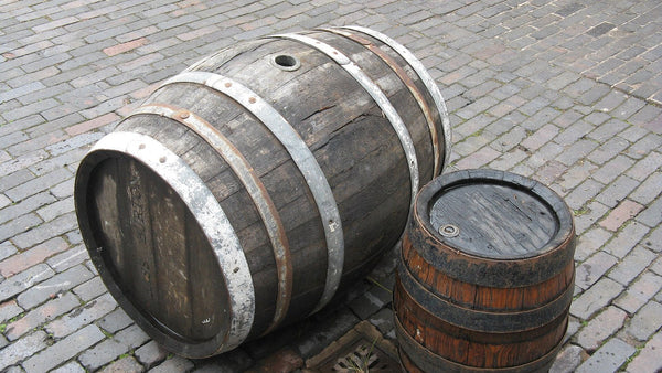 A single weathered oak cask lying on cobblestones next to a small keg.
