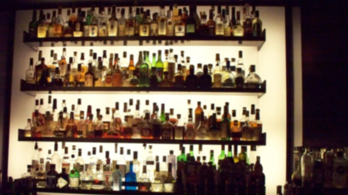 Backlit shelves of liquor bottles behind a dim bar, labels softened out of focus.