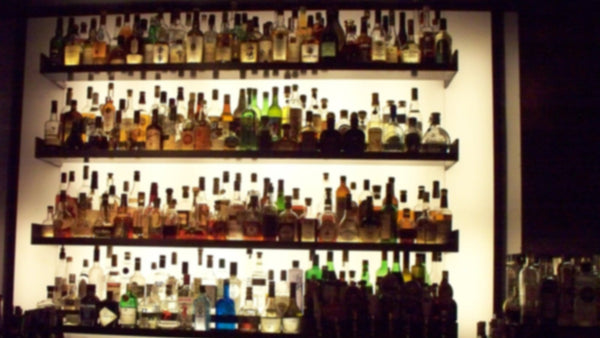 Backlit shelves of liquor bottles behind a dim bar, labels softened out of focus.