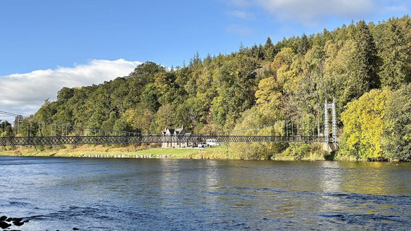 The River Spey flowing past autumn woodland and a suspension footbridge at Aberlour.