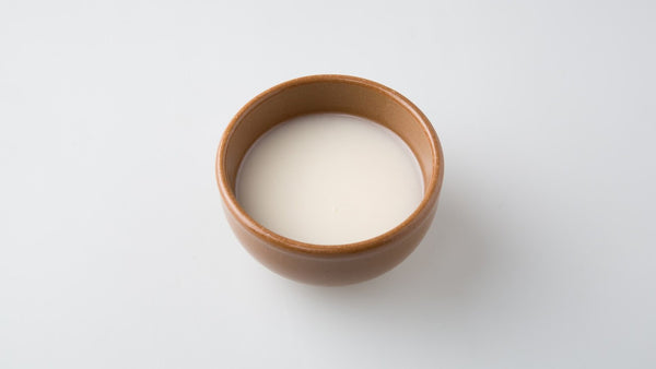A brown ceramic bowl of milky white makgeolli on a plain white surface.