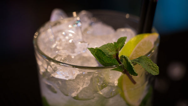 Close-up of an alcohol-free drink over crushed ice, garnished with a sprig of mint and a lime wedge, against a dark bar.