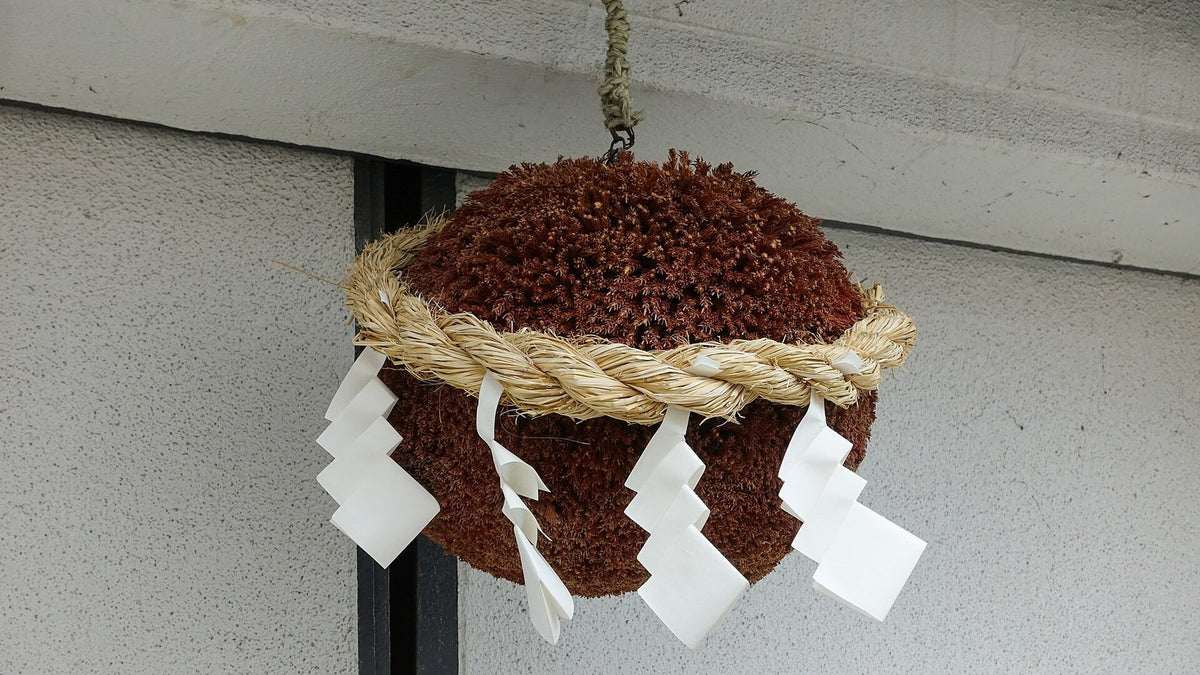 A cedar-ball sugidama with straw rope and white paper streamers hanging outside a sake brewery.