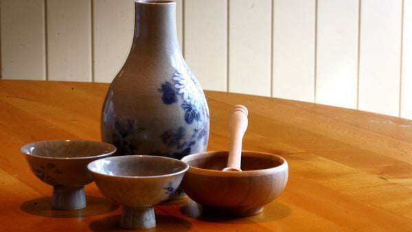 A blue-and-white porcelain bottle with two footed ceramic cups and a wooden bowl on a wooden table.