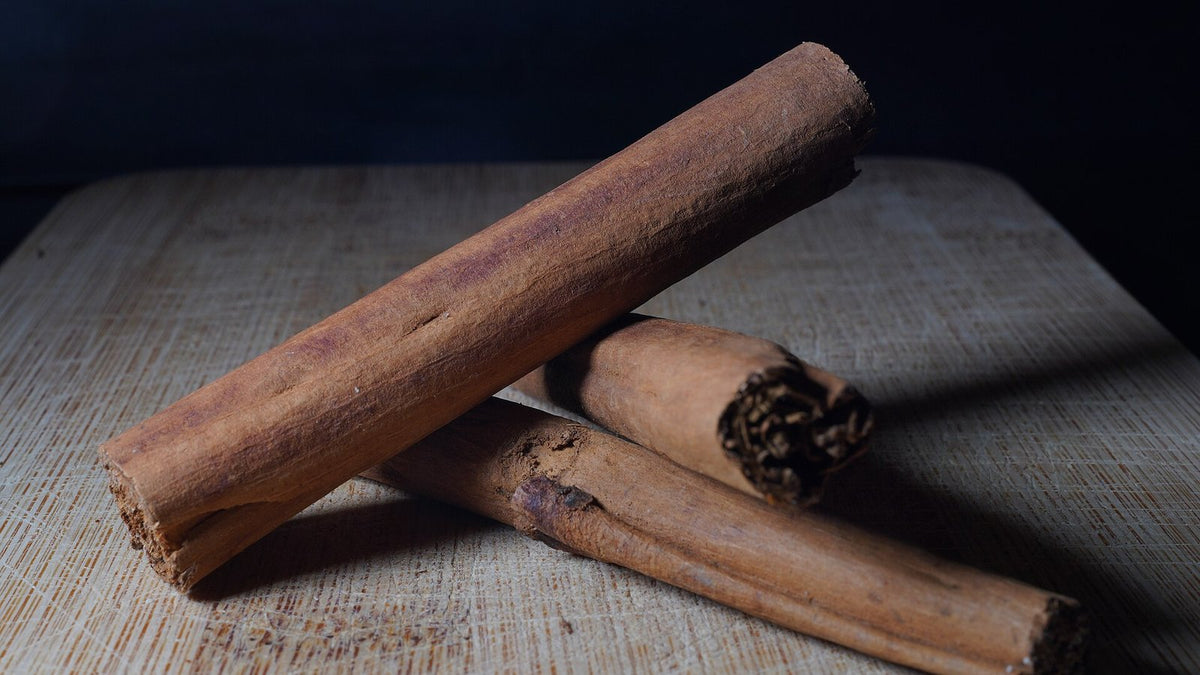 Whole cinnamon sticks lying on a wooden board against a dark background.