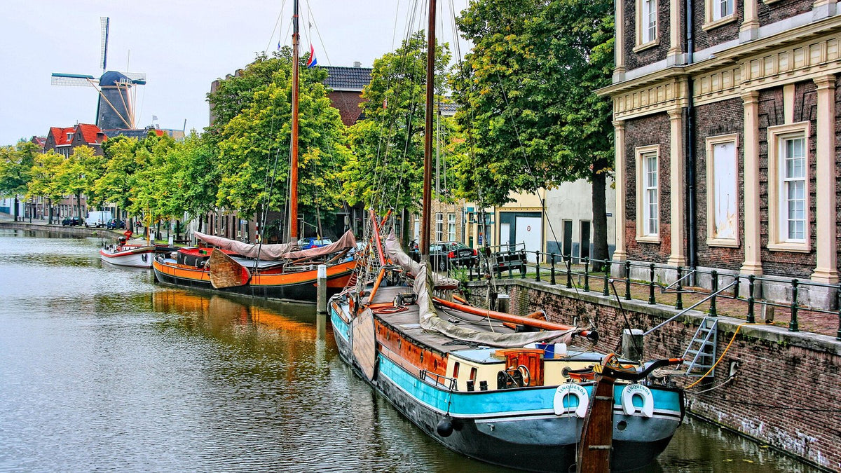 A canal in Schiedam, the Dutch jenever-distilling town, with moored barges, brick buildings and a tall windmill.