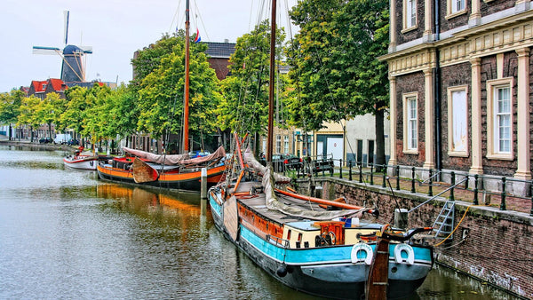 A canal in Schiedam, the Dutch jenever-distilling town, with moored barges, brick buildings and a tall windmill.